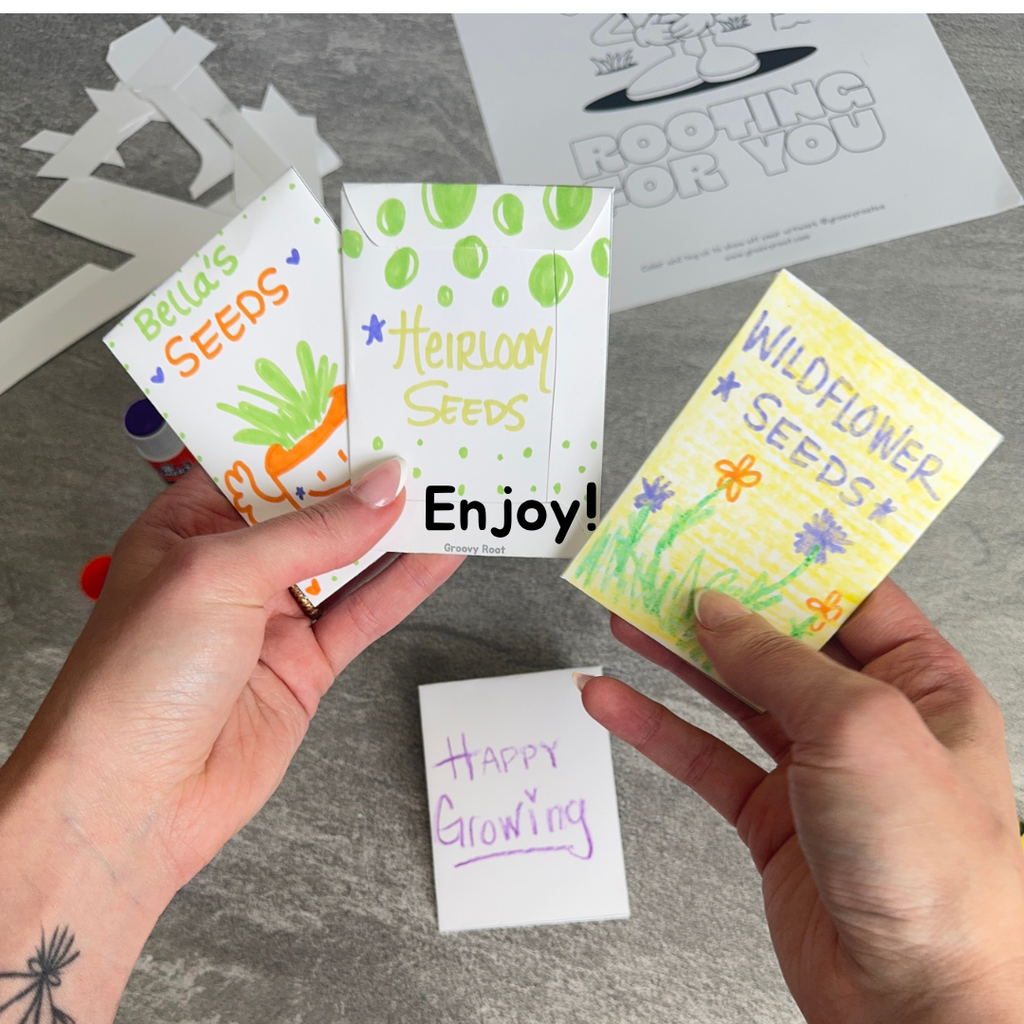 Three small packets of seeds with colorful labels held by hands on a gray surface.