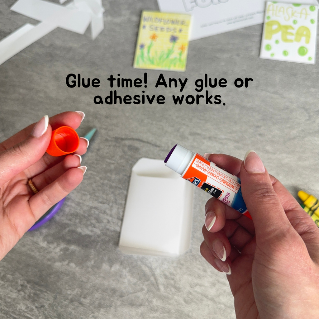 Person holding a glue stick and a small container of glue on a gray surface.
