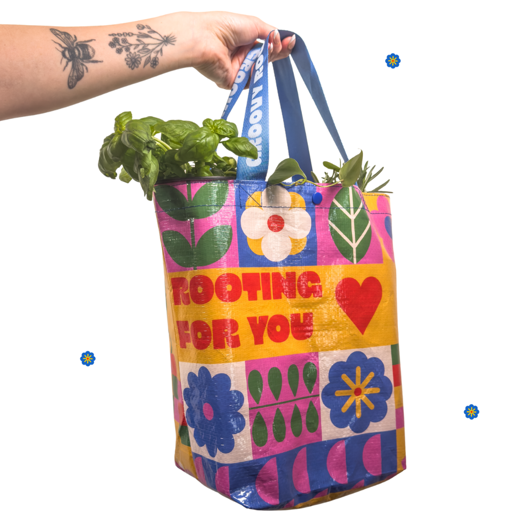 Colorful tote bag with floral patterns and text, held by a person with plants inside.