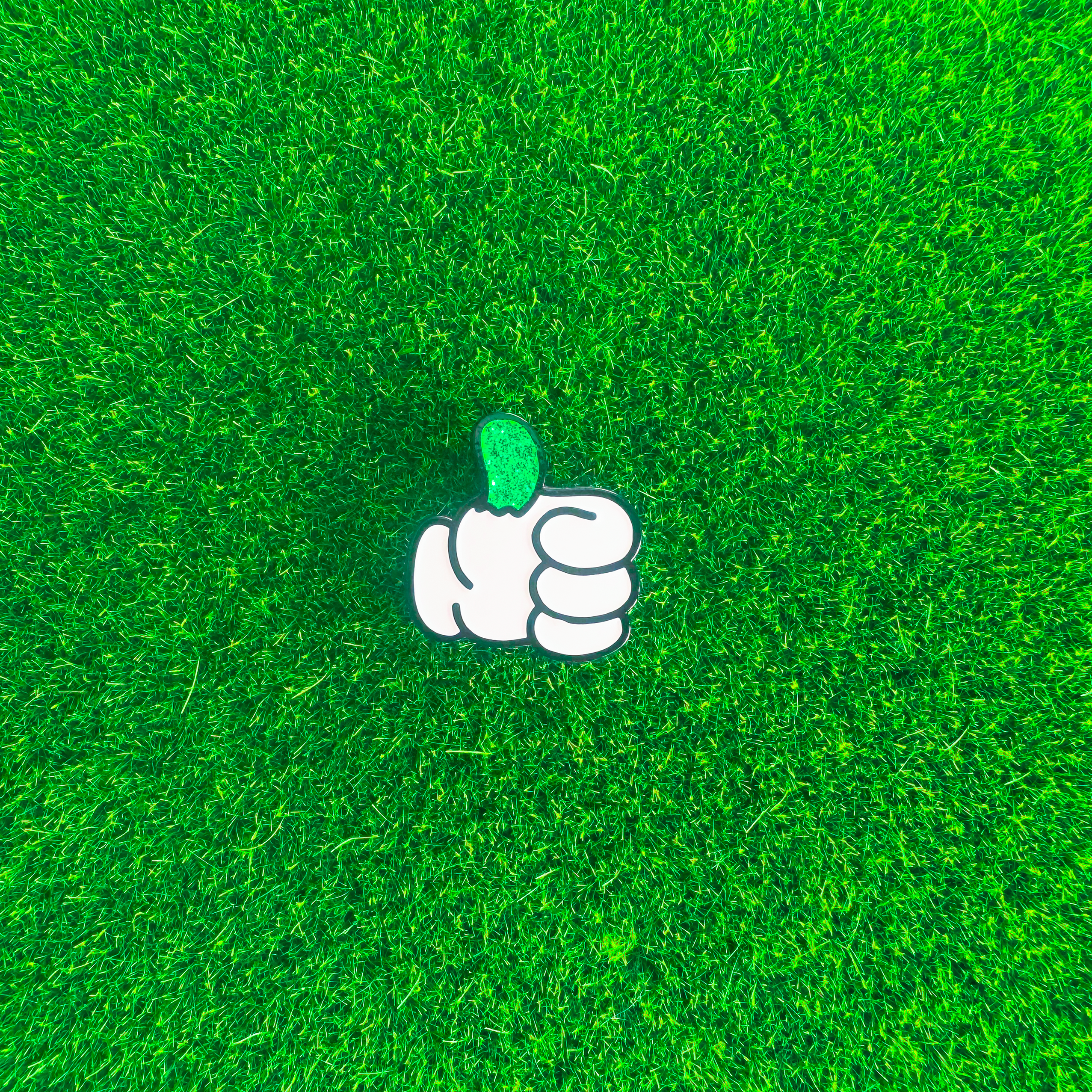 White cartoon hand with a glittery green thumb on a green textured background