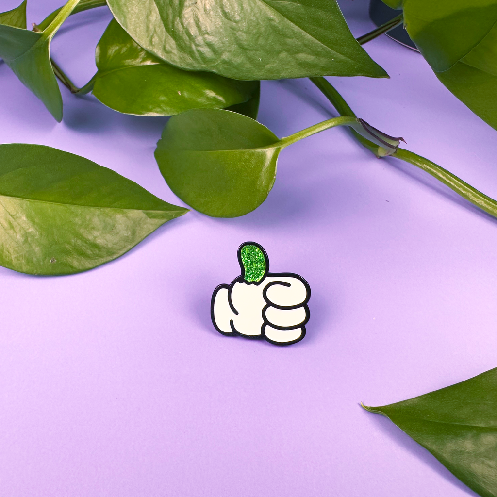 White cartoon-style hand giving a thumbs-up with green leaf on a purple background with leaves.