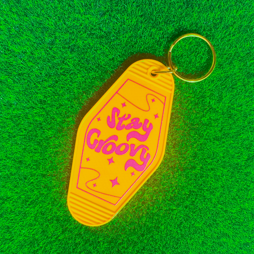 Yellow motel keychain with 'Stay Groovy' text on a green textured background