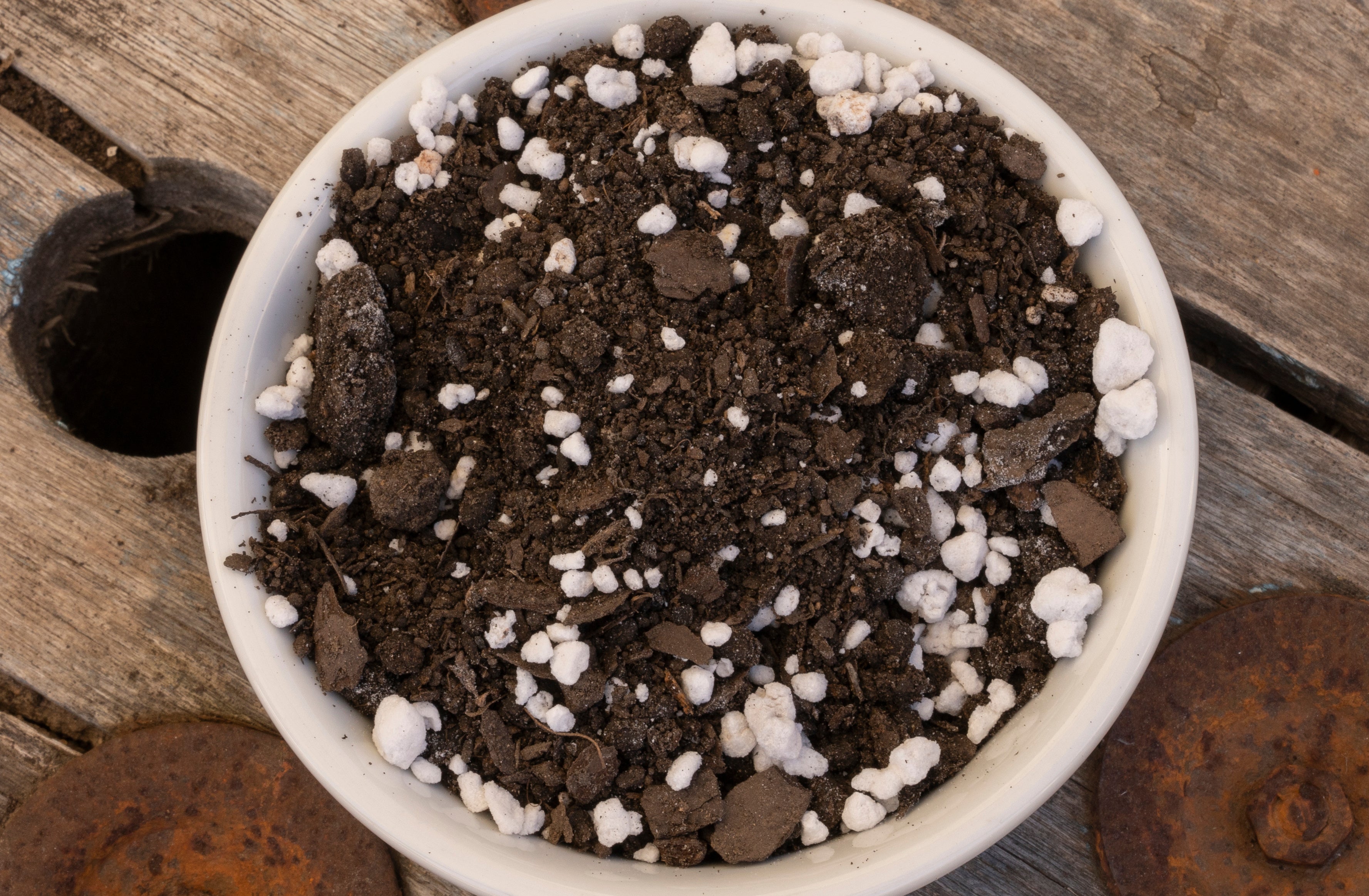 Small white pot filled with soil and small white stones on a wooden surface
