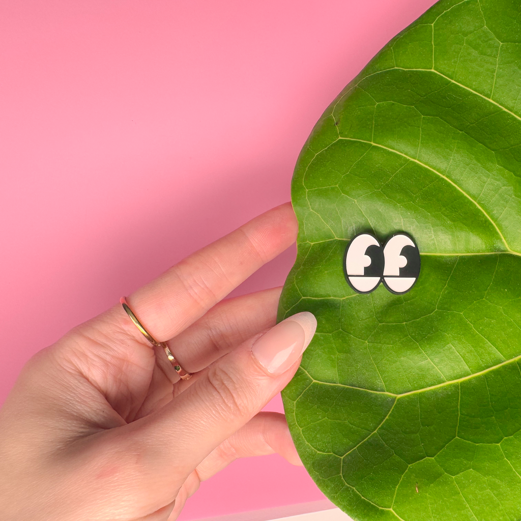 Hand holding a leaf with cartoonish eyes on a pink background