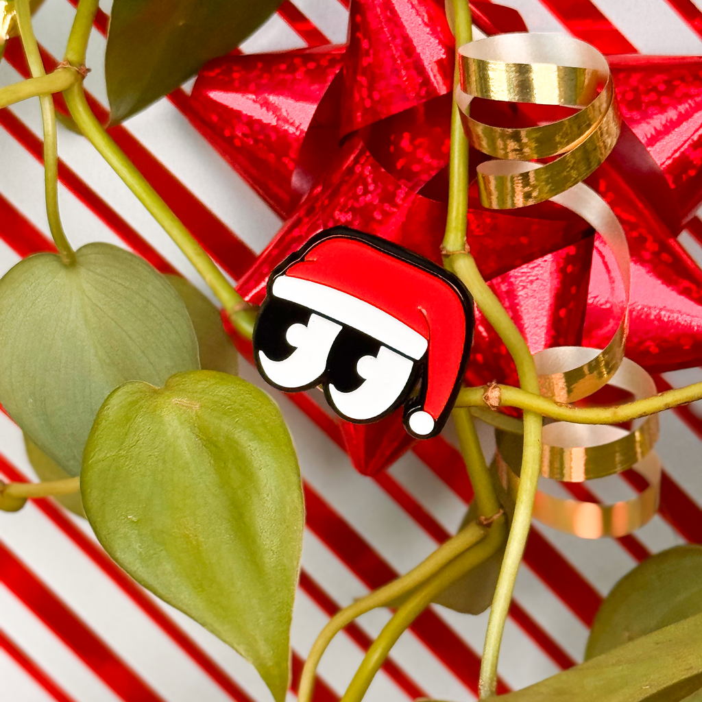 Red gift with gold ribbon and Santa hat on a red and white striped background