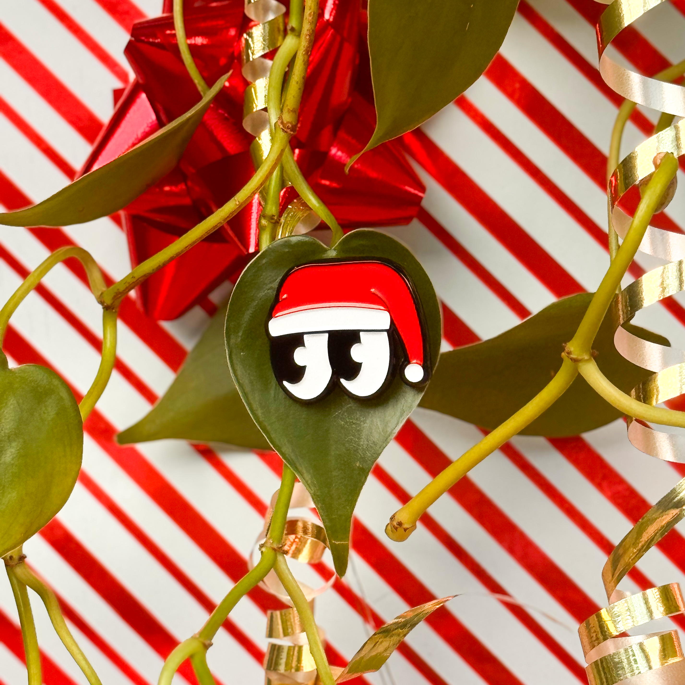 Decorative mistletoe with cartoon eyes wearing a santa hat magnetized to a plant leaf. 