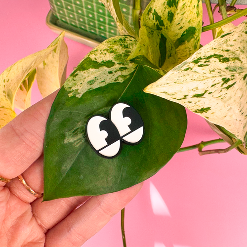 Hand holding a leaf with a black and white logo on a pink background