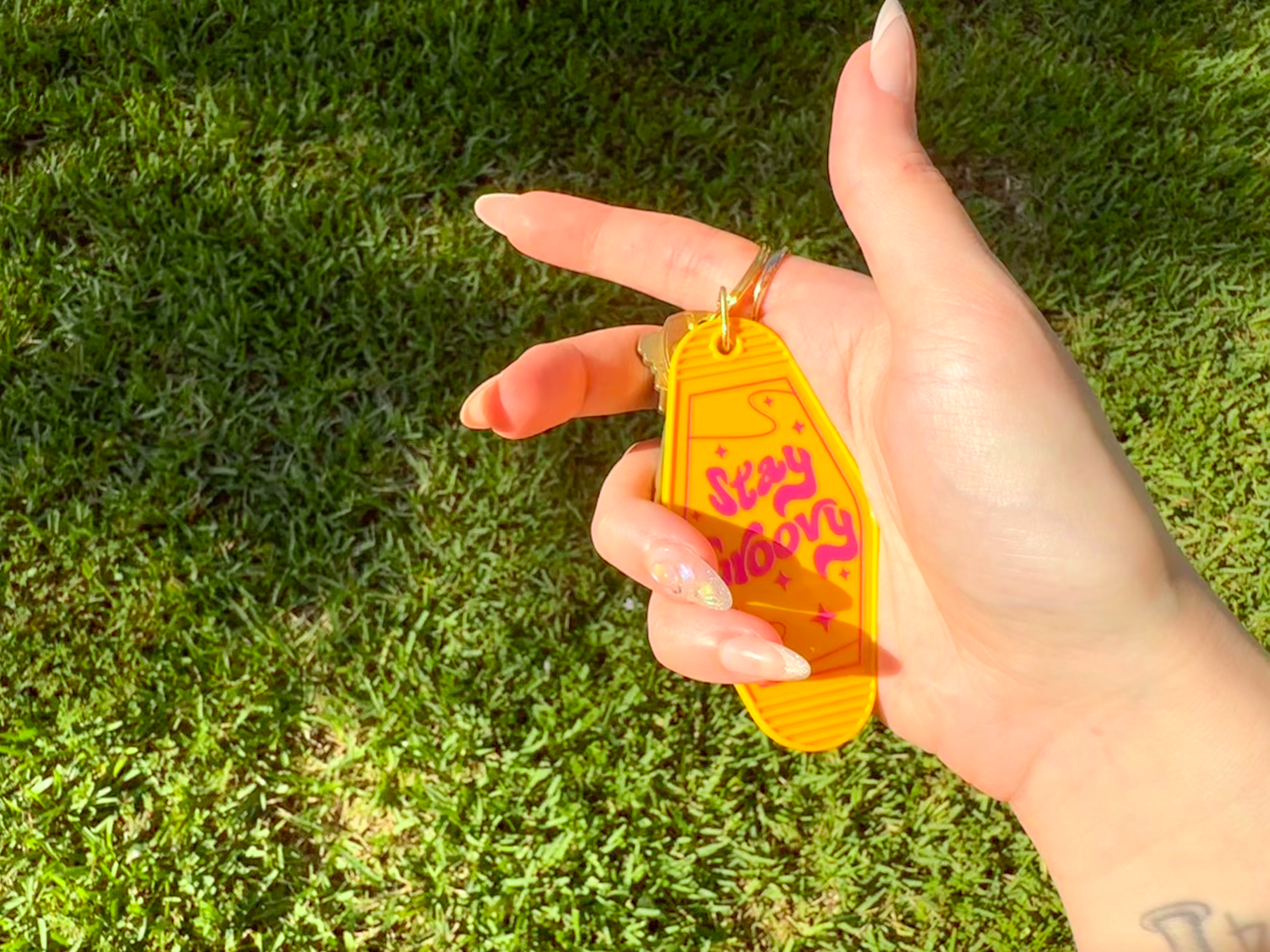 Hand holding a yellow keychain with 'Stay Home' text on grass background