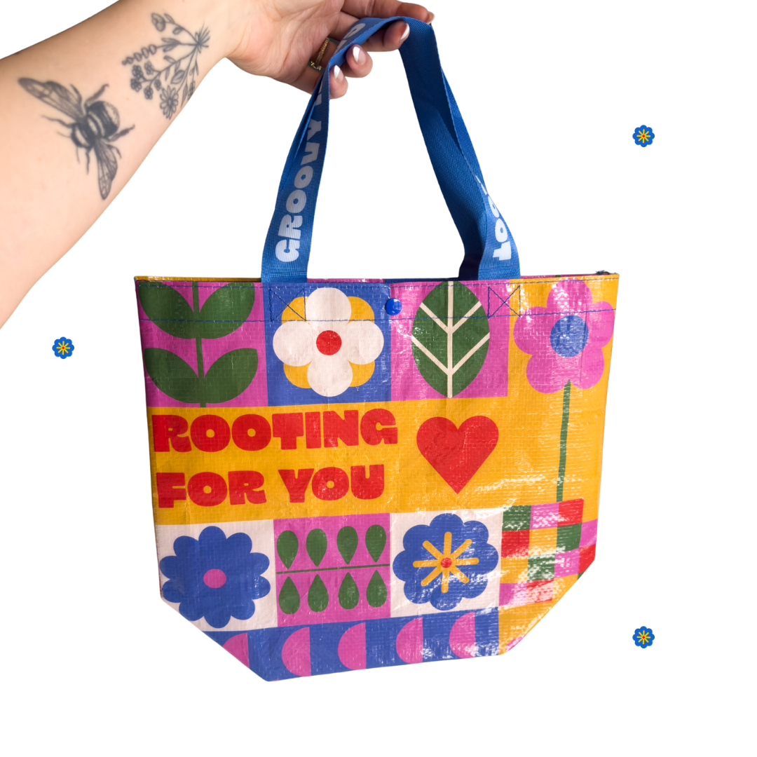 Colorful tote bag with floral patterns and text held by a hand on a white background