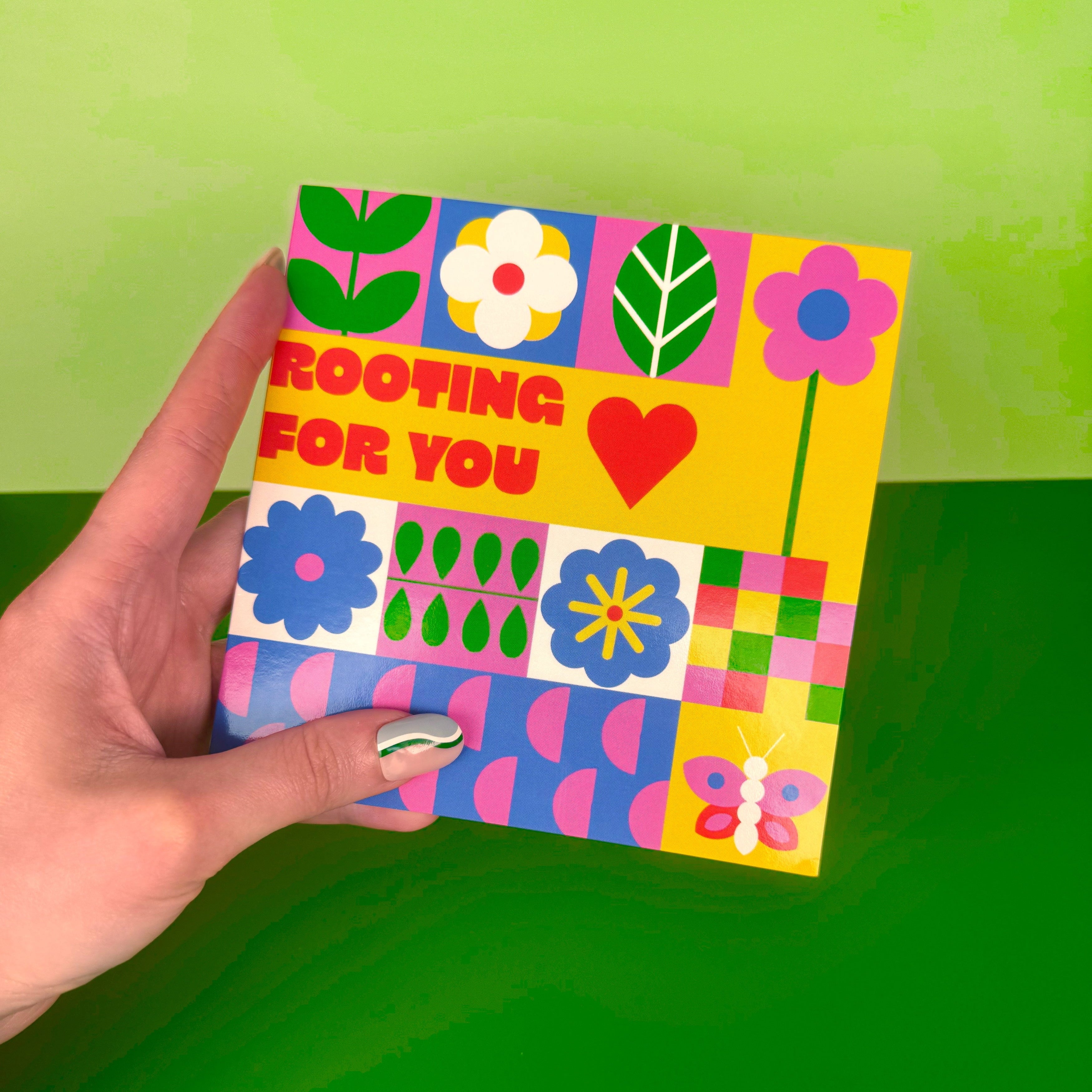 Colorful card with floral designs and text held by a hand against a green background